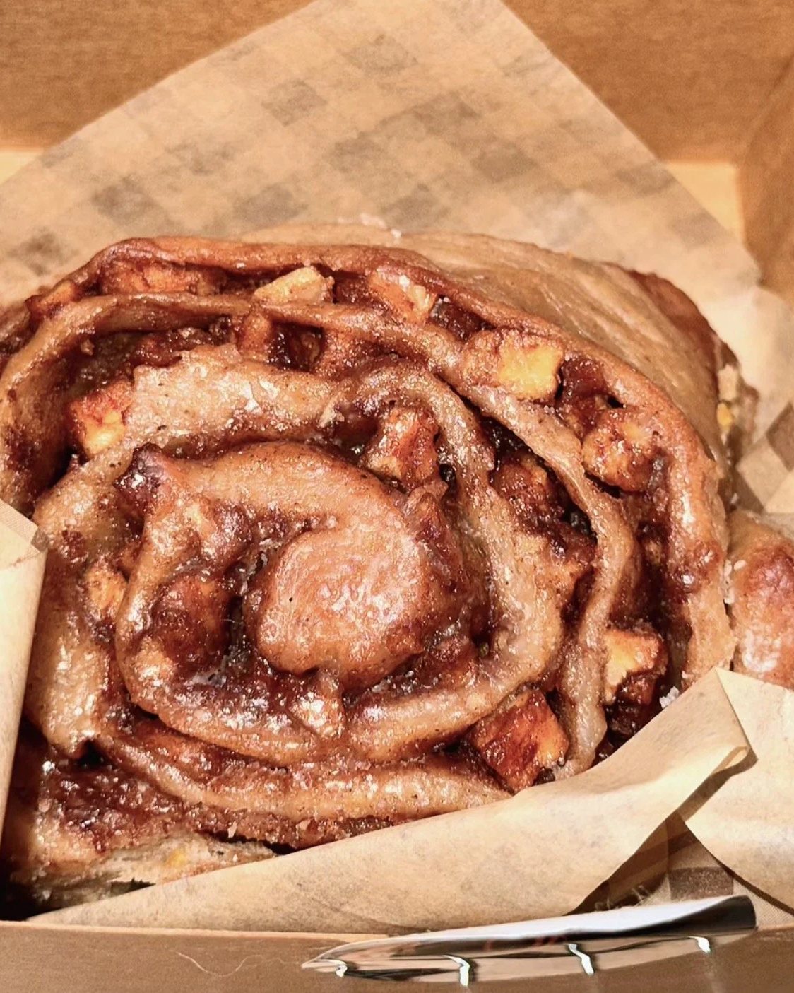 A glazed Southern cinnamon roll in a kraft box lined with gingham paper
